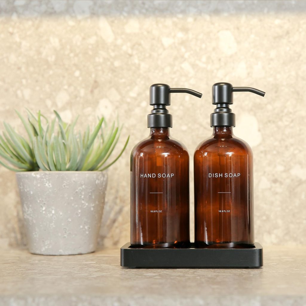 2 amber glass soap dispenser bottles staged on a bathroom counter next to a plant